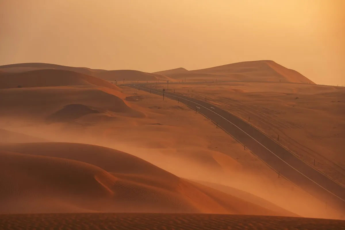 Empty highway curving through desert dunes at sunset