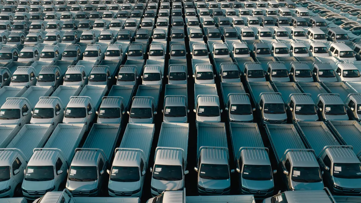 Aerial view of a large fleet of identical white pickup trucks parked in rows